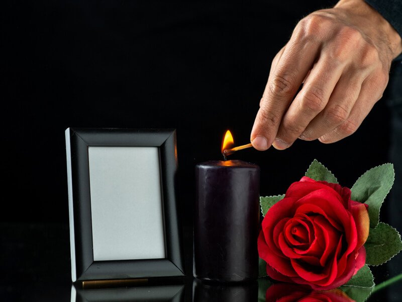 Front view of dark candle with red rose and picture frame on dark surface