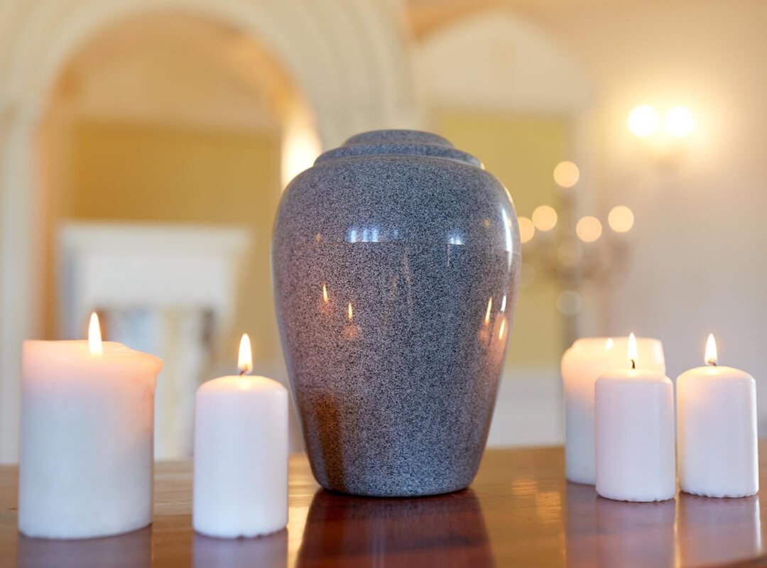 Funeral, cremation and mourning concept - funerary urn and candles on table burning in church